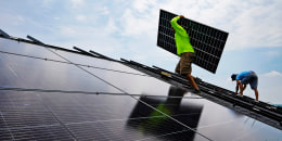 Nicholas Hartnett, owner of Pure Power Solar, carries a panel as he and Brian Hoeppner install a solar array on the roof of a home in Frankfort, Ky., on July 17, 2023.
