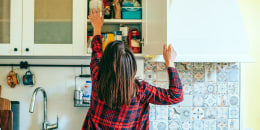 Rear view of a woman reaching inside her kitchen cabinet.
