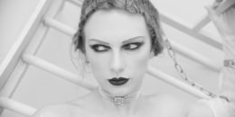 Swift with her hair in pincurls, thin eyebrows, dark lipstick is chained to a bed.