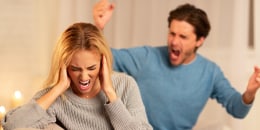 Abusive Husband Shouting At Wife Sitting On Couch At Home