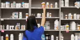 A pharmacy technician grabs a bottle of drugs off a shelf at a pharmacy