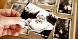 Mature person's hand holding an old photograph of young baby.