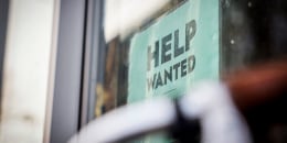 A HELP WANTED sign is posted at a storefront.