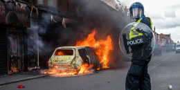 A police officer stands near a burning car on the road