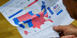 A man holds a printed page showing a map with electoral vote data.