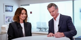 Demi Lovato, left, watches as Gavin Newsom signs a document next to her while at a table