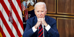 President Joe Biden is seated at a desk, with his chin rested atop his clasped hands