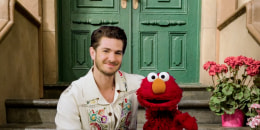 Andrew Garfield and Elmo sit on a stoop