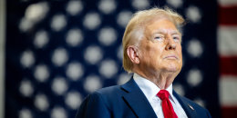 Donald Trump on stage in front of an American flag backdrop