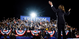 Kamala Harris onstage with her back to the camera raise her hands to greet the audience