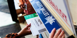 A hand places a ballot into a ballot box