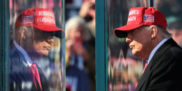 Donald Trump looks out towards an audience past protective glass that reflects him