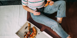 An Unrecognizable Woman Eating Pizza And Drinking Beer While Sitting On The Floor