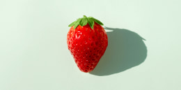 Strawberry in the middle of a soft green background with natural light and long shadows.