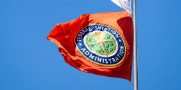 A red Federal Aviation Administration flag flies from a poles, with a white flag on top of it