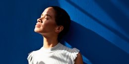 Thoughtful woman standing against blue wall.