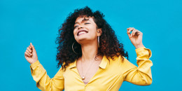Shot of a young woman dancing and smiling while standing against a blue background.