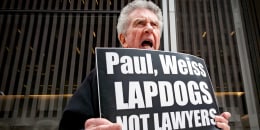 A protester holds a sign that reads, "Paul, Weiss Lapdogs not lawyers"
