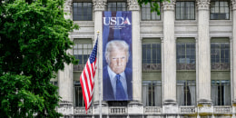 A building with a portrait of Donald Trump draped on the outside, next to an American flag
