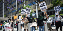 Protestors hold anti-ICE signs on the sidewalk outside of a building