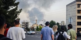 Smoke rises in the distance as people look on