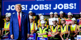 Donald Trump stands on stage in front of workers wearing safety vests