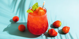 Summer refreshing sparkling drink with melted ice, fresh strawberry and drinking straw and mint in transparent glasses on blue background.