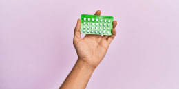 Young hispanic hand holding birth control pills over isolated pink background.