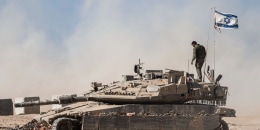 An Israeli soldier stands on the top of a tank parked