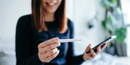 Woman smiling happily, using ovulation tracker apps on smartphone to check the pregnancy test result.