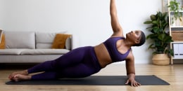 Young black woman doing side plank yoga pose at home