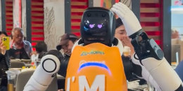A robot wears an orange apron and has two hearts for eyes