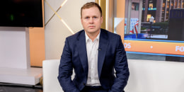 Spencer Pratt seated on a white couch with his hands folded in his lap.