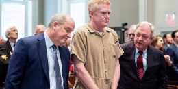 Alex Murdaugh stands handcuffed between two lawyers in a courtroom.