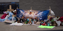 A memorial with balloons and stuffed animals in front of a Walmart.