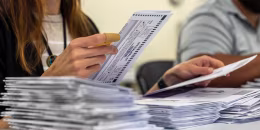 A woman extracts a mail-in ballot from an envelope. 