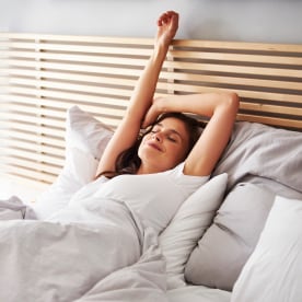 Woman stretching in bed with comforter and pillows