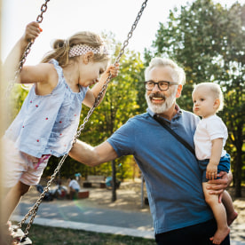 Grandfather Having Fun With Grandchildren On Swings