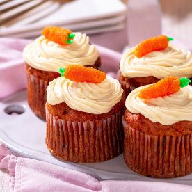 Carrot cake muffins with cream cheese, topped with marzipan carrots on a plate. Delicious homemade dessert.