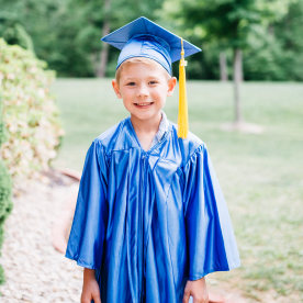 Portrait of happy boy in graduation gown standing at park