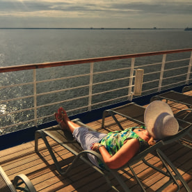 A middle aged woman in a sunbonnet relaxes on the top deck of a cruise ship during her vacation at sea