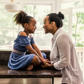 Image: A mother and young daughter laughing in a kitchen.