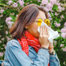 Young asian woman sneezes and blowing her nose with a handkerchief and suffering in the spring among flowering and blooming trees.