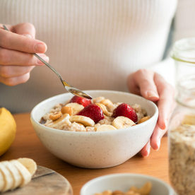 Woman putting together oatmeal with banana, strawberries and nuts.