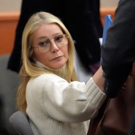 Paltrow in a white turtleneck sweater and aviator-style glasses frowns at something off-screen.