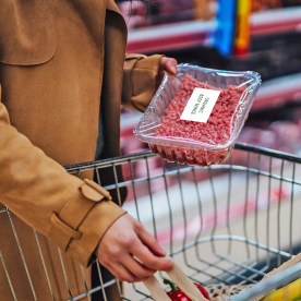 Young woman placing a pack of fresh minced beef in shopping cart.