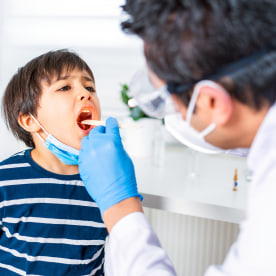 Pediatrician examining child patient’s throat at clinic.