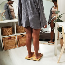 Young plus size woman in grey shirt standing on scales