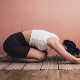 An anonymous woman holding the child's pose while doing yoga on a mat.