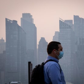 A man wears a face mask as smoke continues to shroud the sun as it rises behind the skyline of Manhattan in New York City on June 7, 2023, as seen from Weehawken, New Jersey.